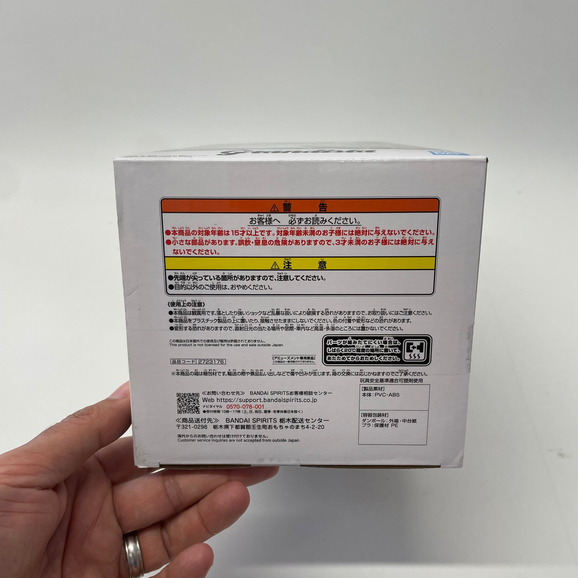 Hand holding a white box with text and a barcode on a light gray background