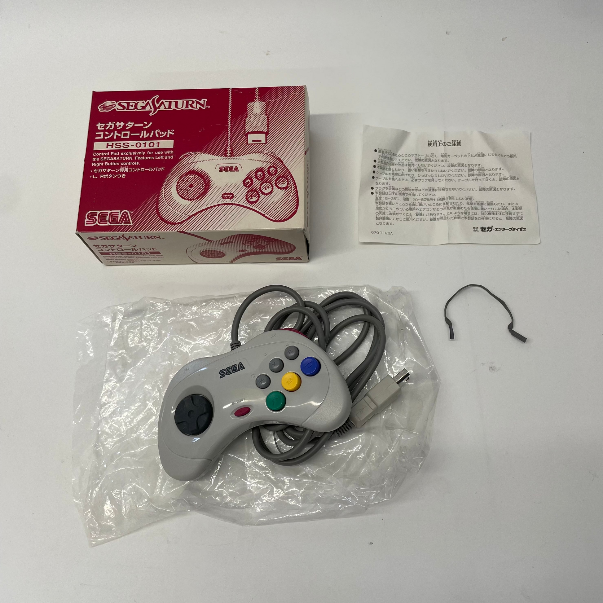 Sega Saturn controller with packaging and manual on a white background