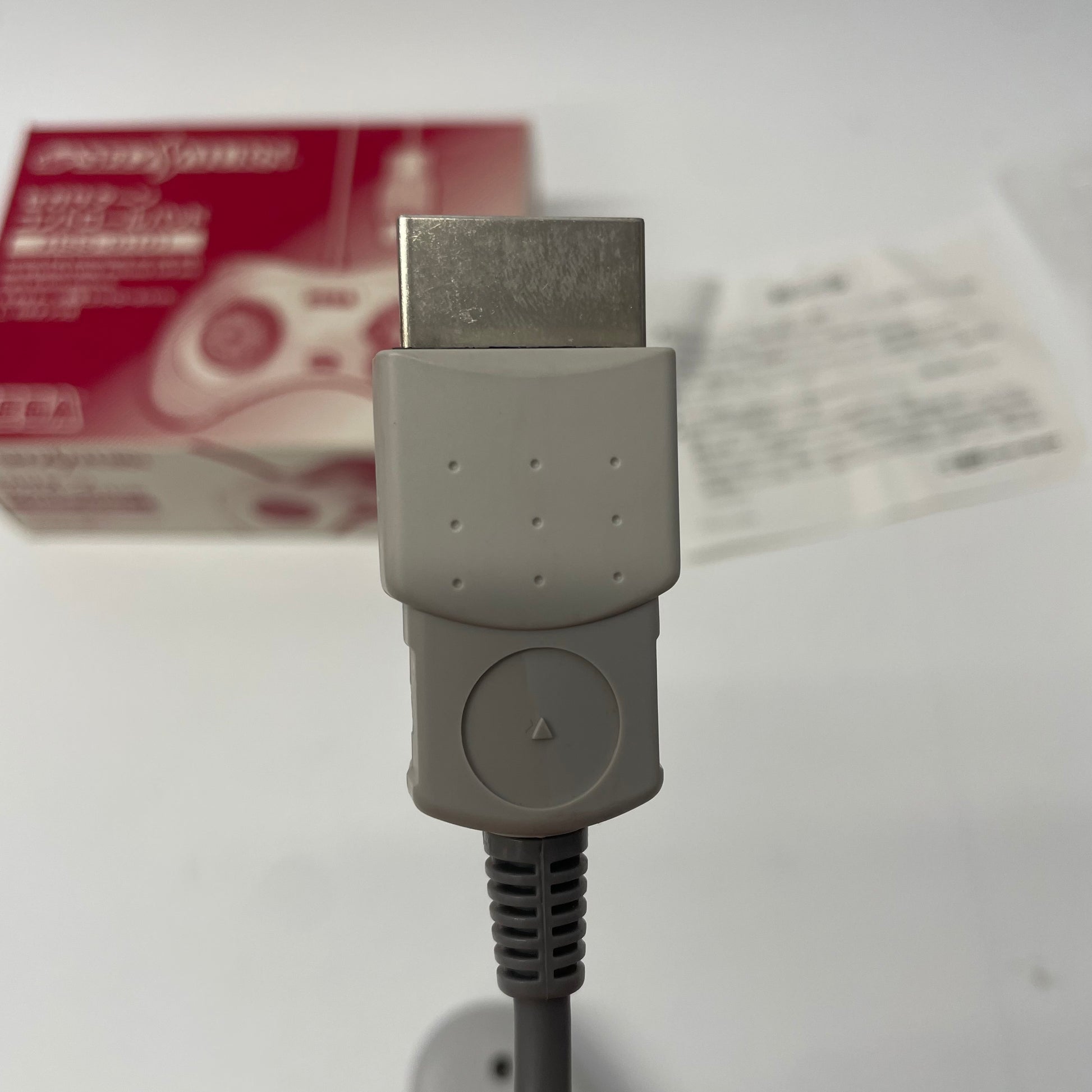 Close-up of a gray HDMI adapter with a blurred Sega Genesis controller box in the background.