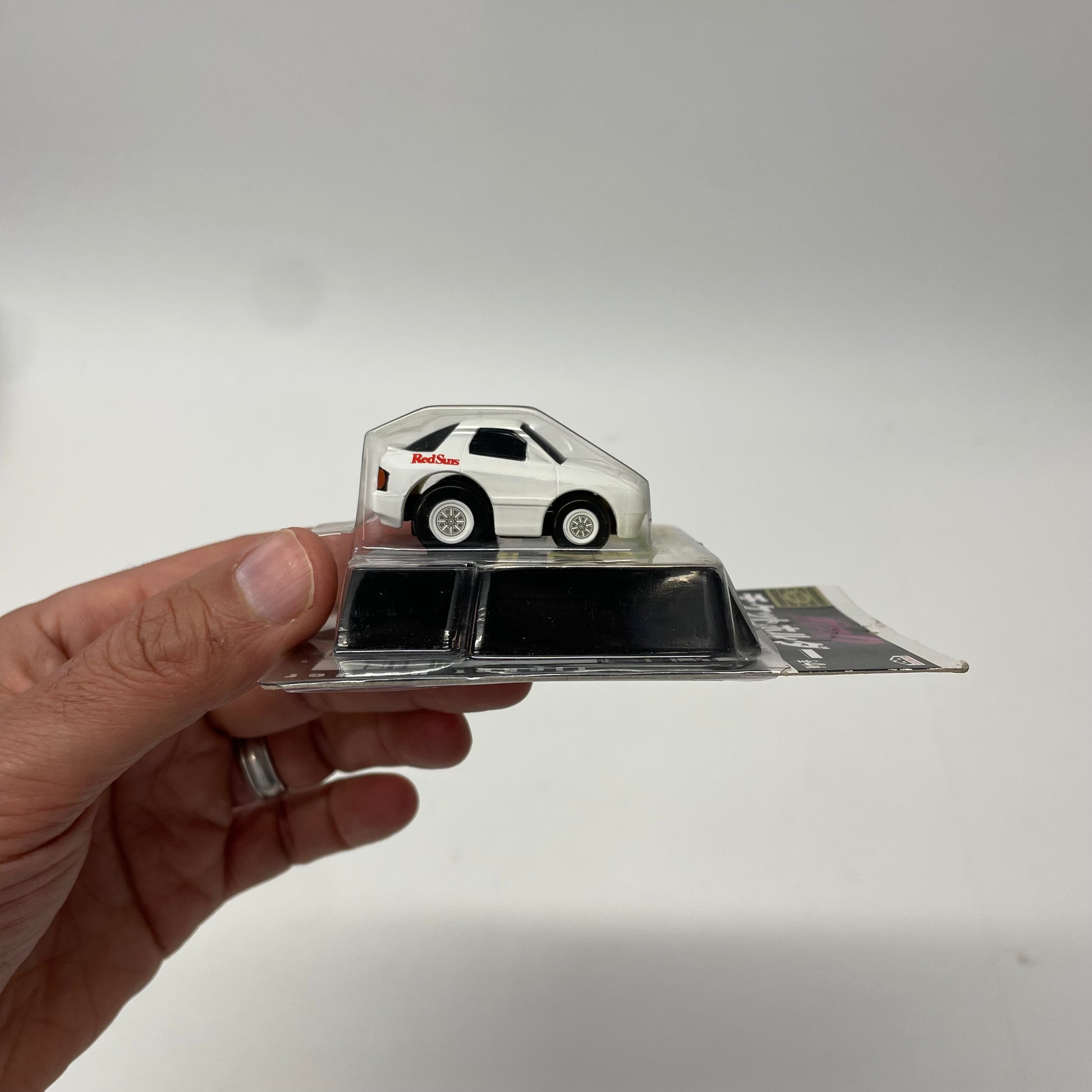 Hand holding a small model car on a clear stand against a plain background
