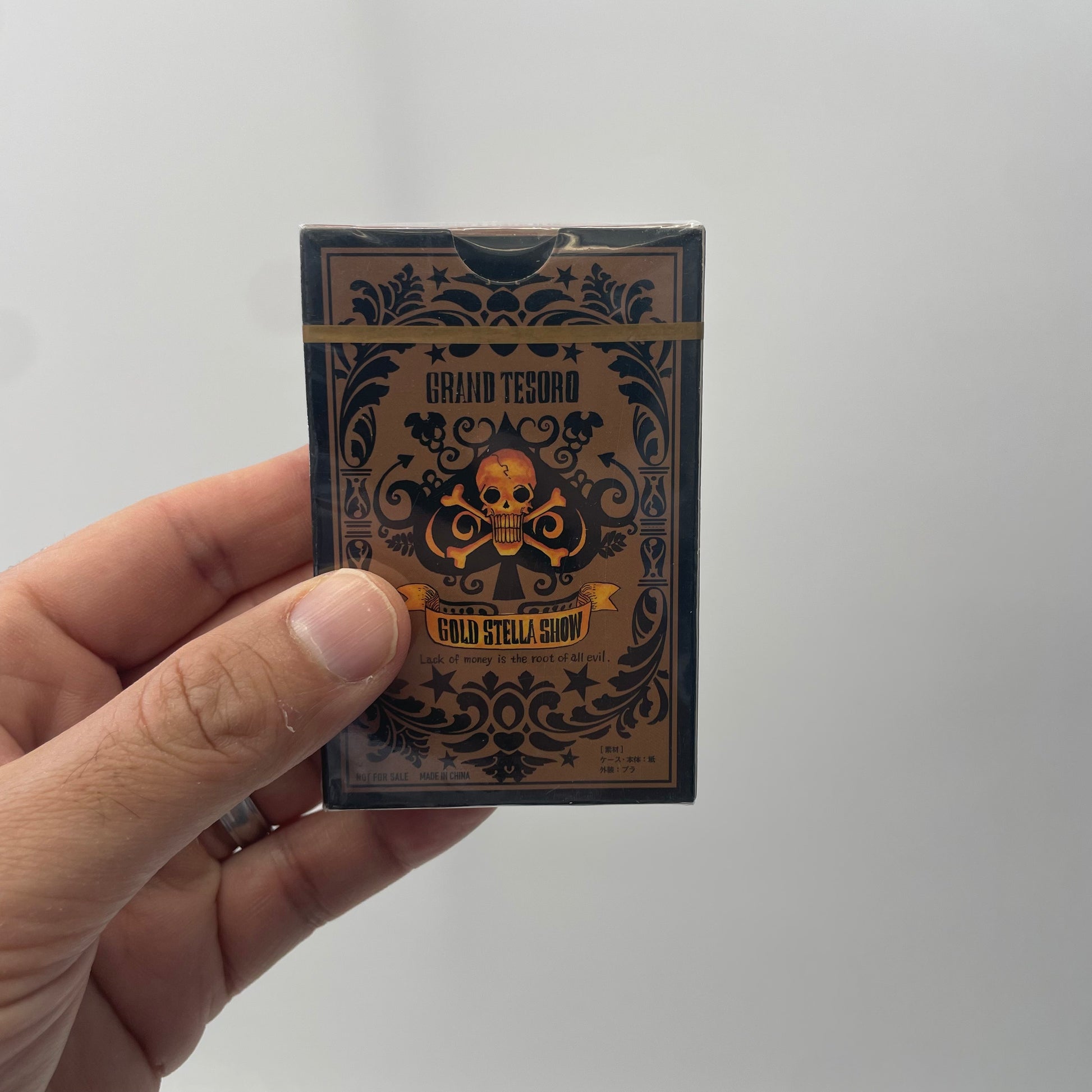 Hand holding a deck of cards with decorative packaging against a plain background