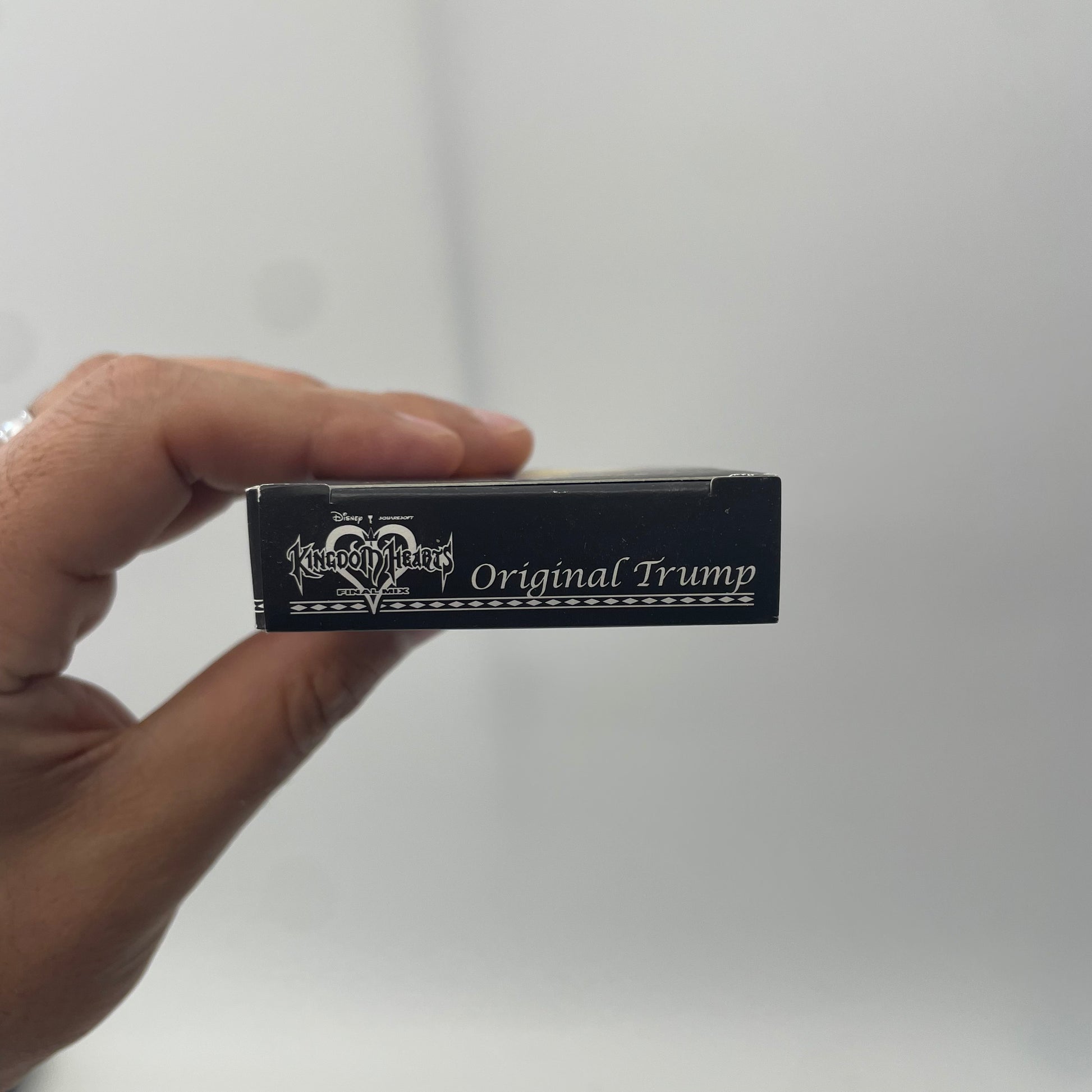 Hand holding a small black box labeled 'Original Trump' against a plain background