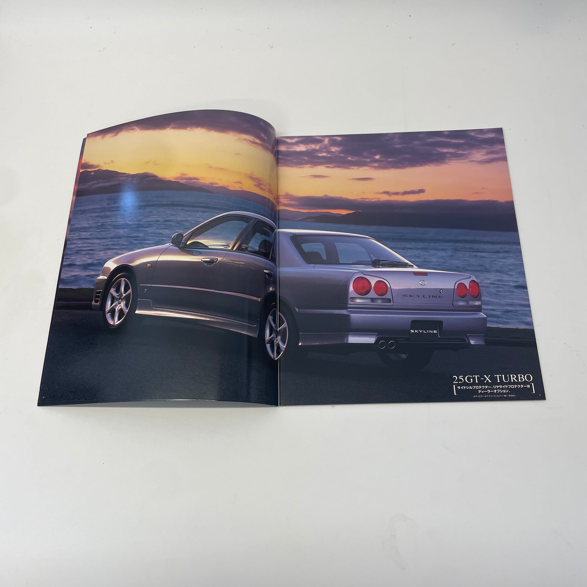 Open car brochure showing a silver car by a lake with a sunset.