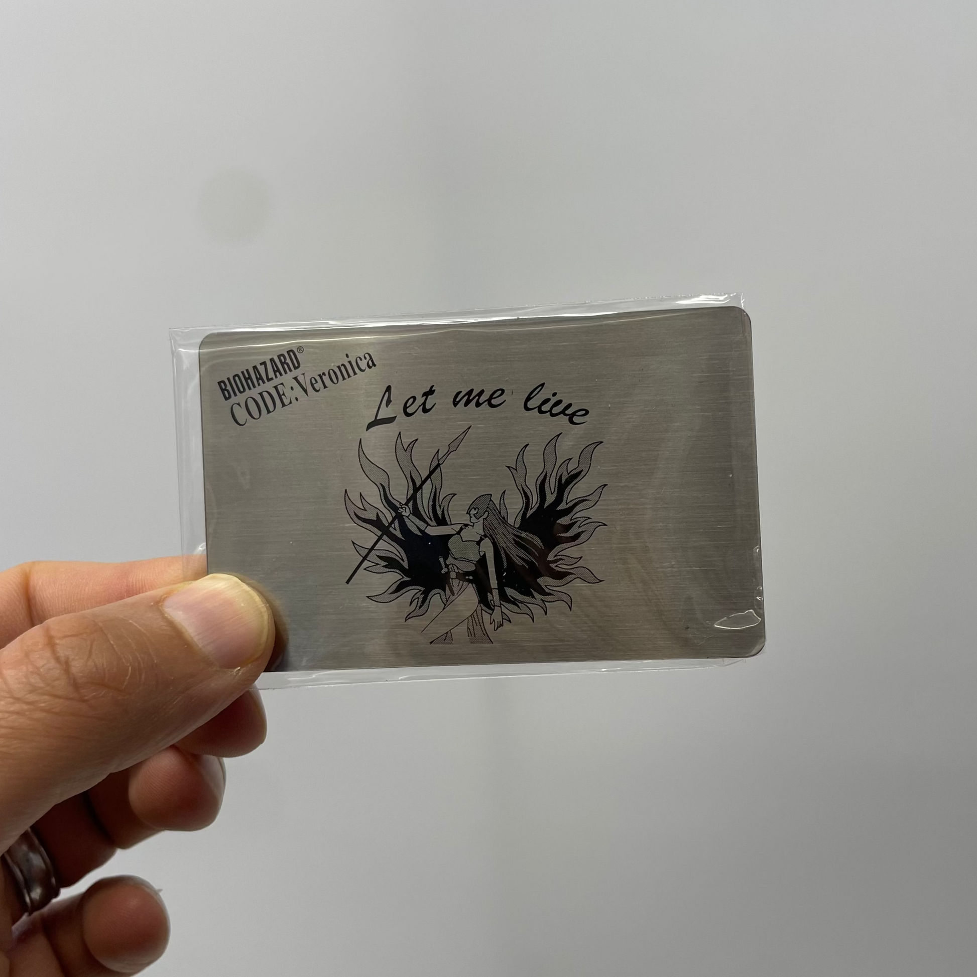 Card with 'Let me live' text and artwork held by a hand against a plain background