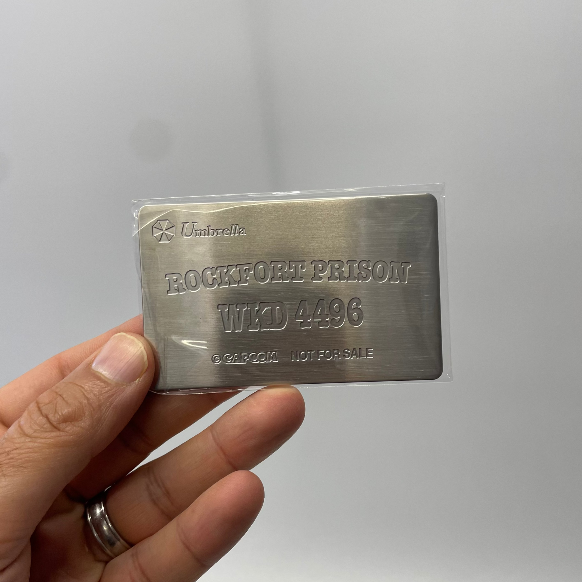 Metal card with engraved text held by a hand against a white background