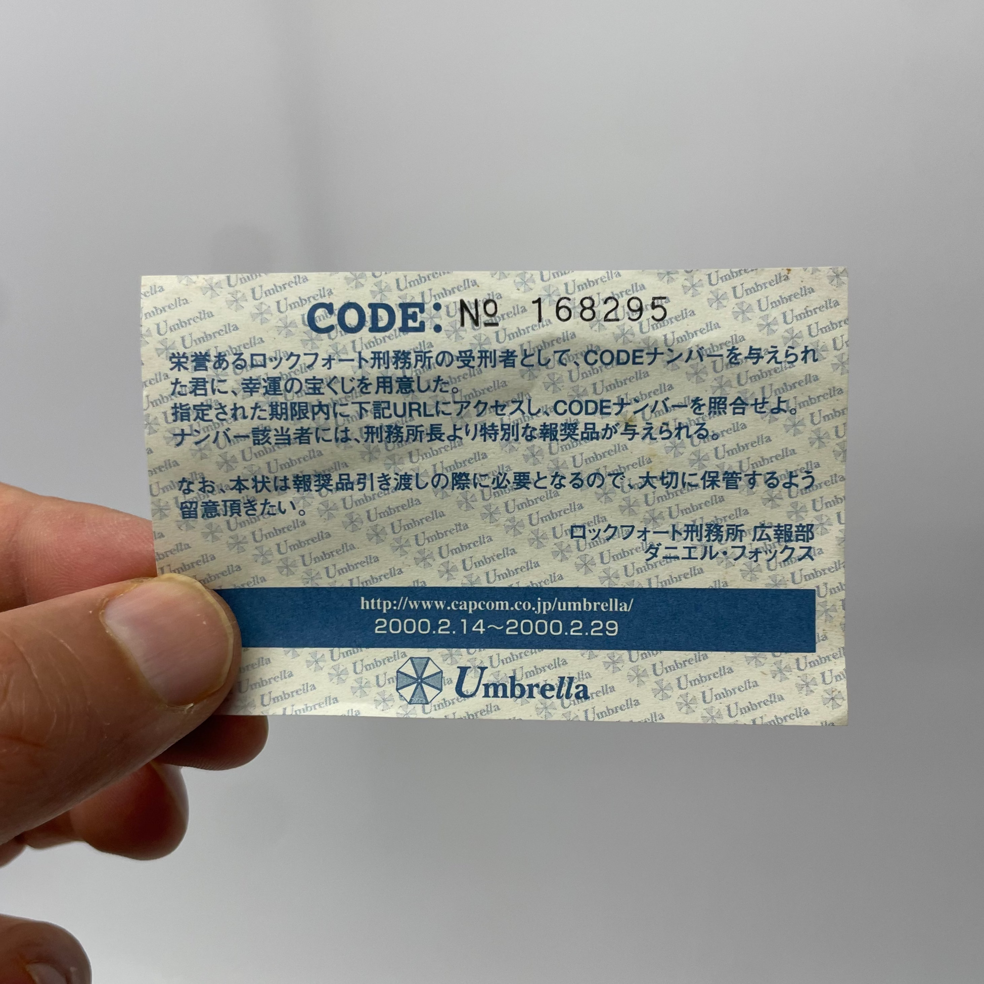 Hand holding a small card with text and branding, featuring the word 'Umbrella'.