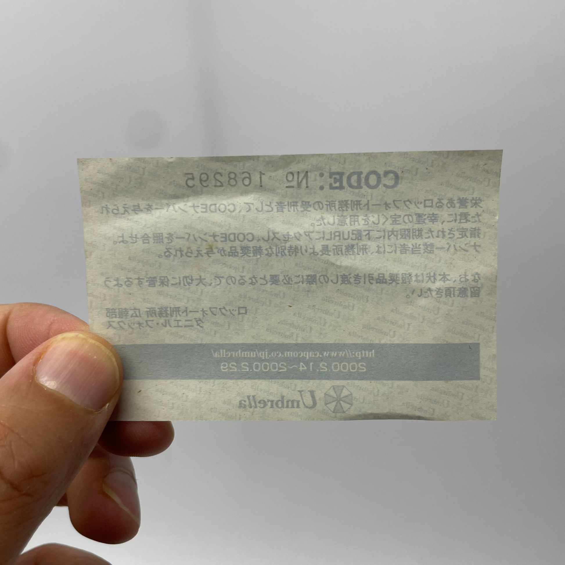 Hand holding a small printed card with text and a code on a plain background