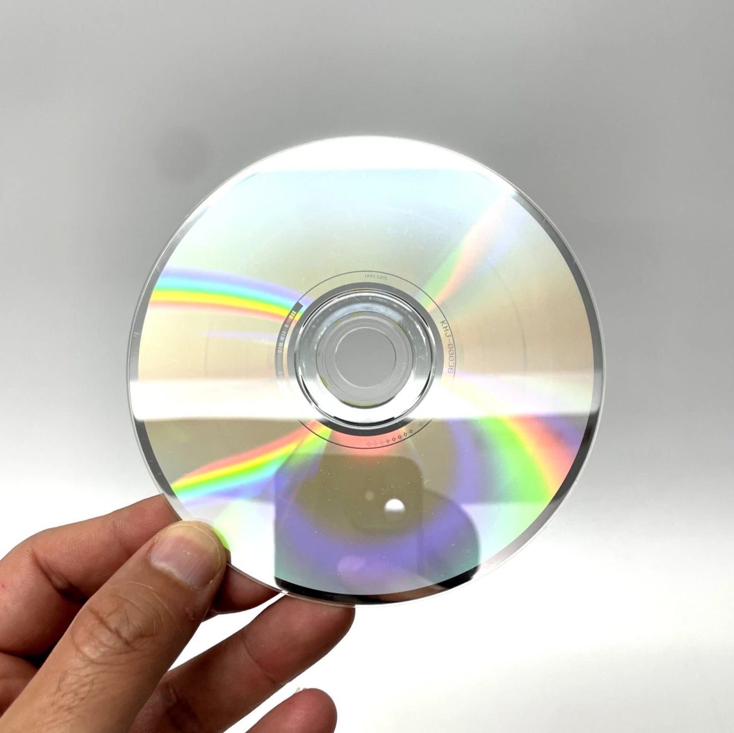 Hand holding a CD with rainbow reflection against a gray background