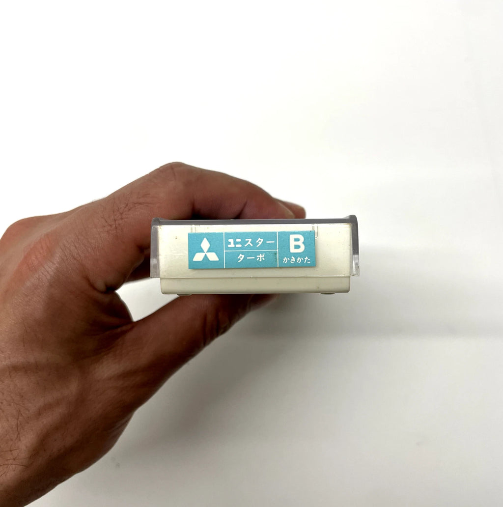 Hand holding a small cylindrical device with Mitsubishi branding on a white background