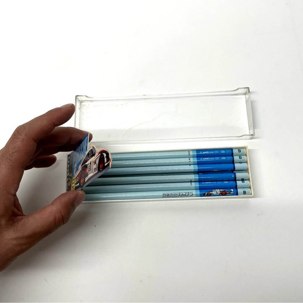 Hand opening a transparent case containing blue and gray pencils on a white background