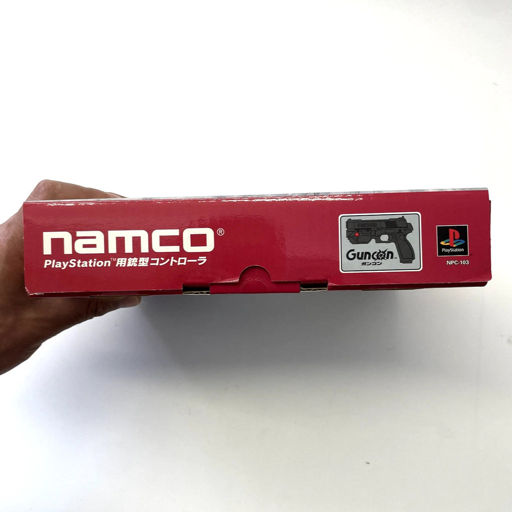 Red box with 'namco' branding held by a hand on a white background