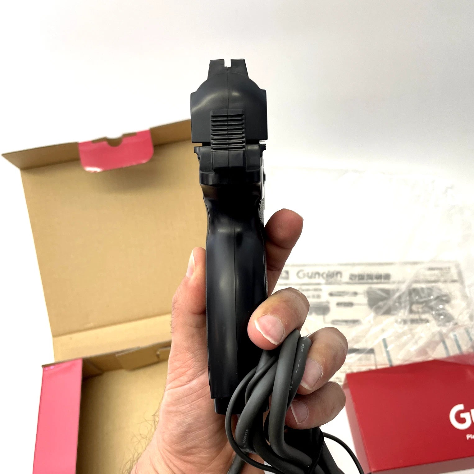 Hand holding a black electronic device with a cardboard box and red item in the background
