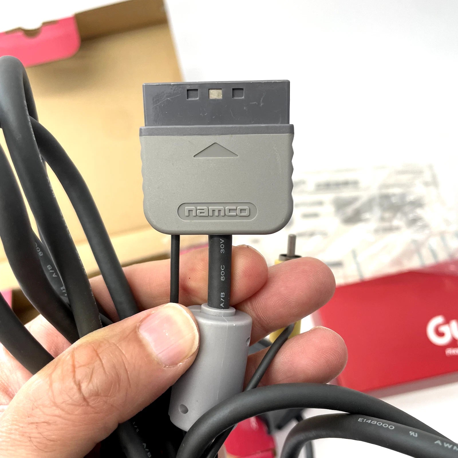 Gray Namco cable adapter held by a hand with a blurred background