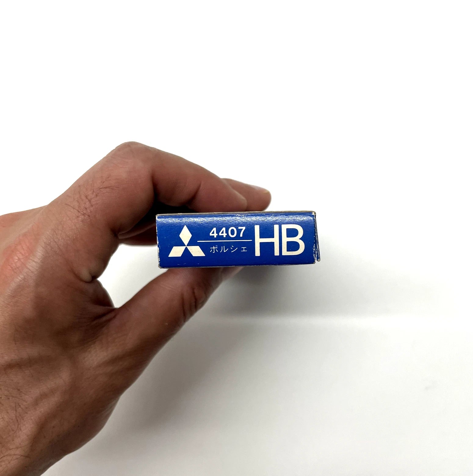 Hand holding a blue Mitsubishi pencil lead with '4407 HB' marking on a white background