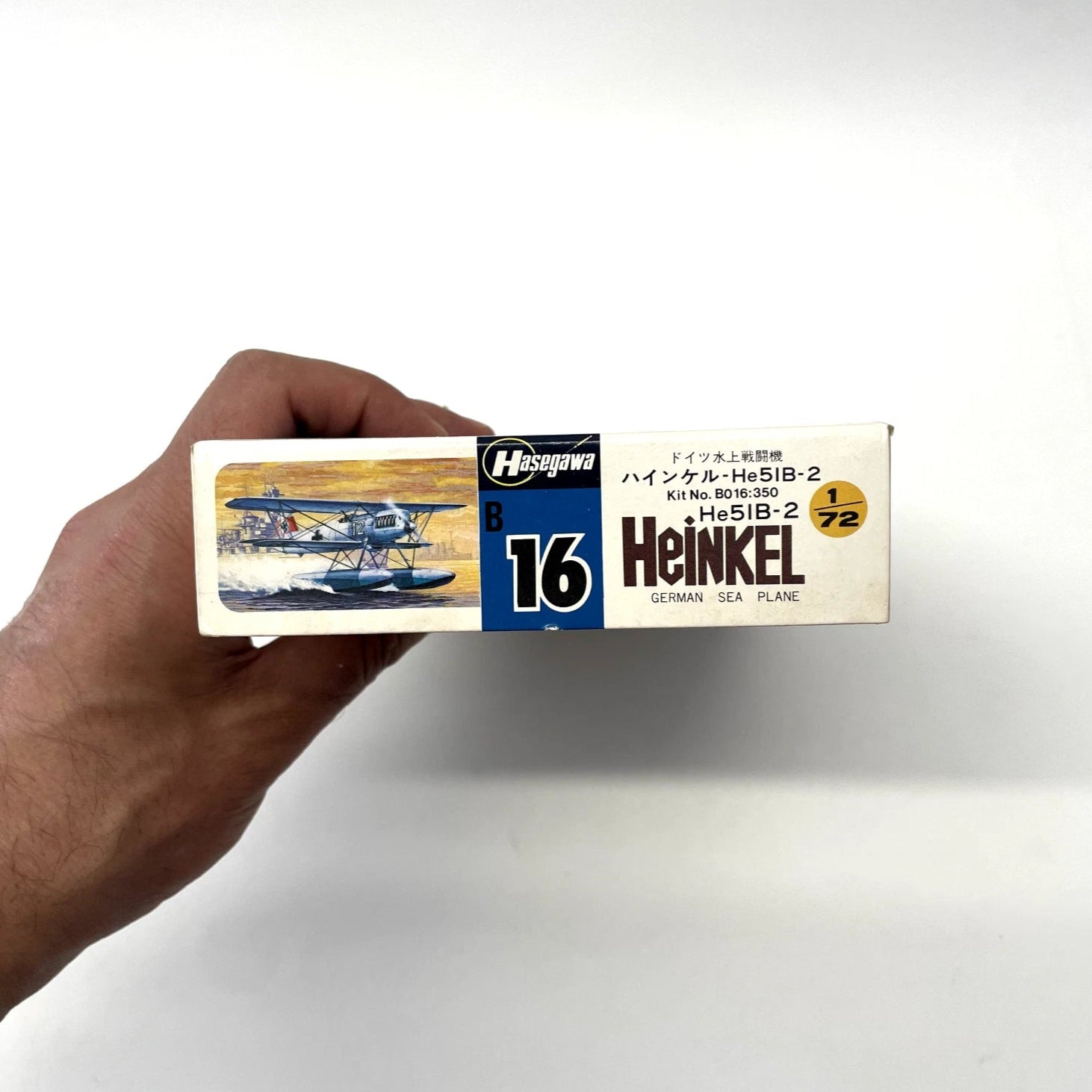 Hand holding a model airplane kit box with 'Heinkel' branding on a white background