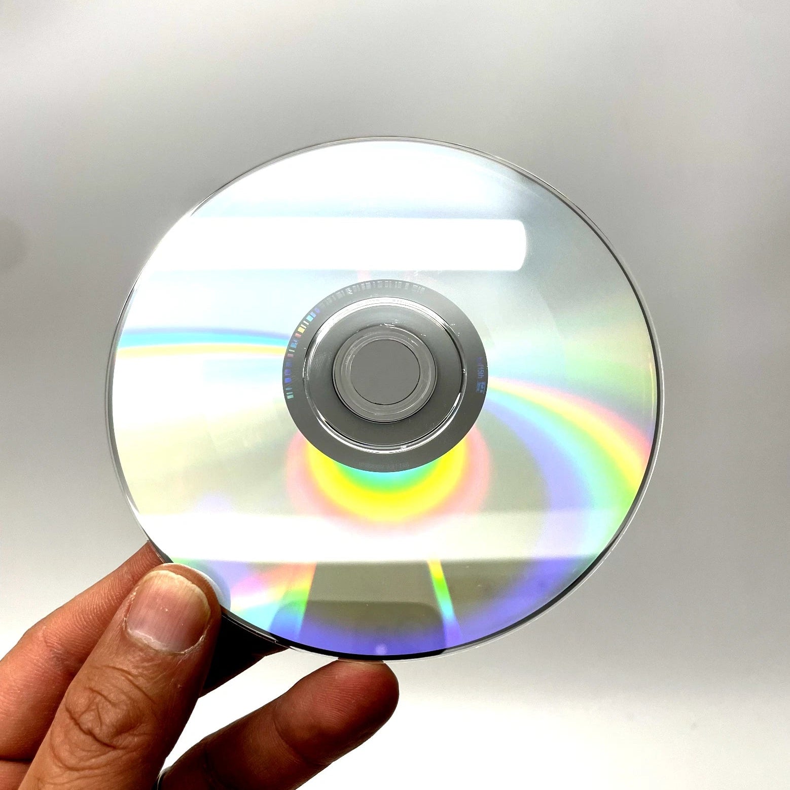 Hand holding a CD with rainbow reflections against a neutral background