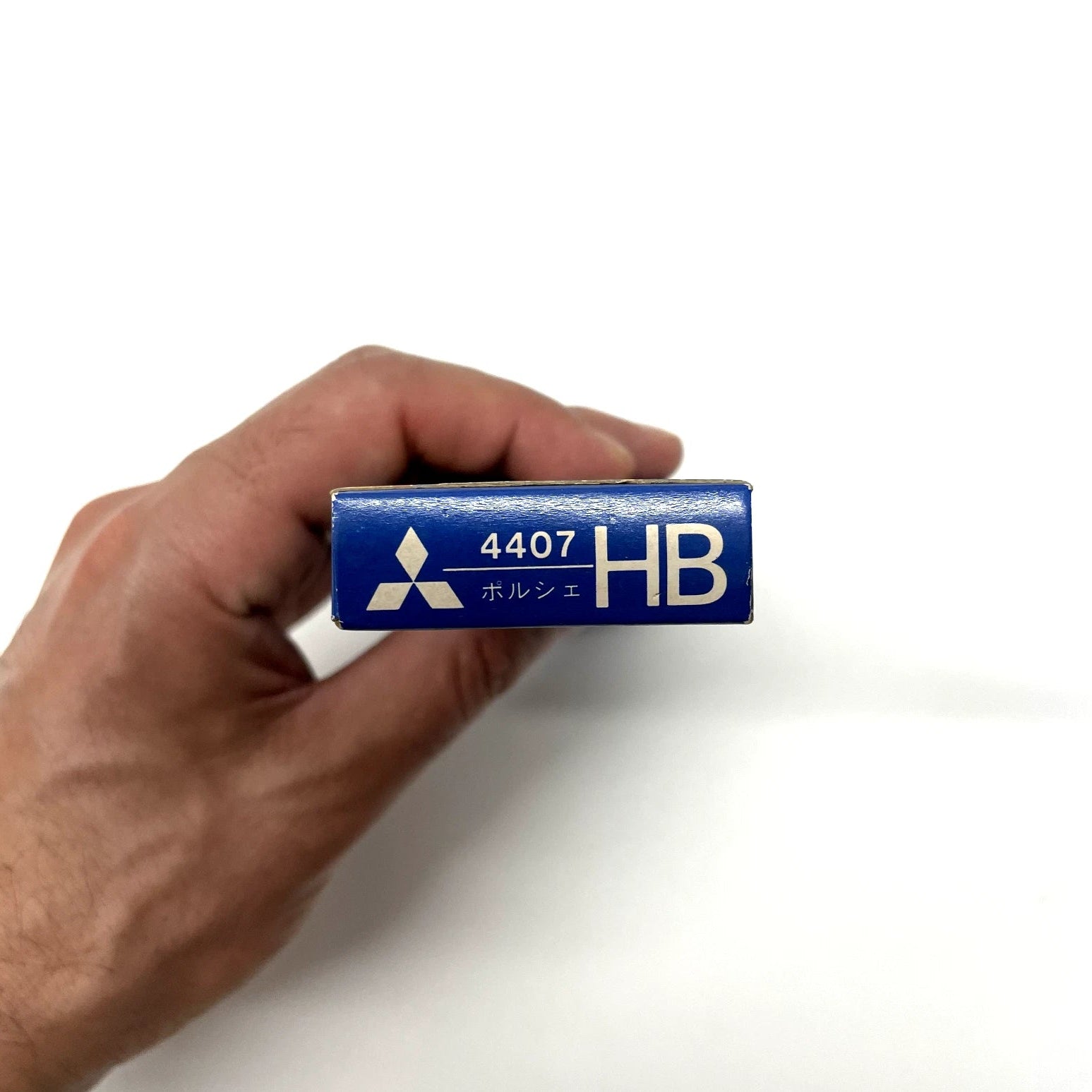 Hand holding a blue mechanical pencil lead container with '4407 HB' marking on a white background