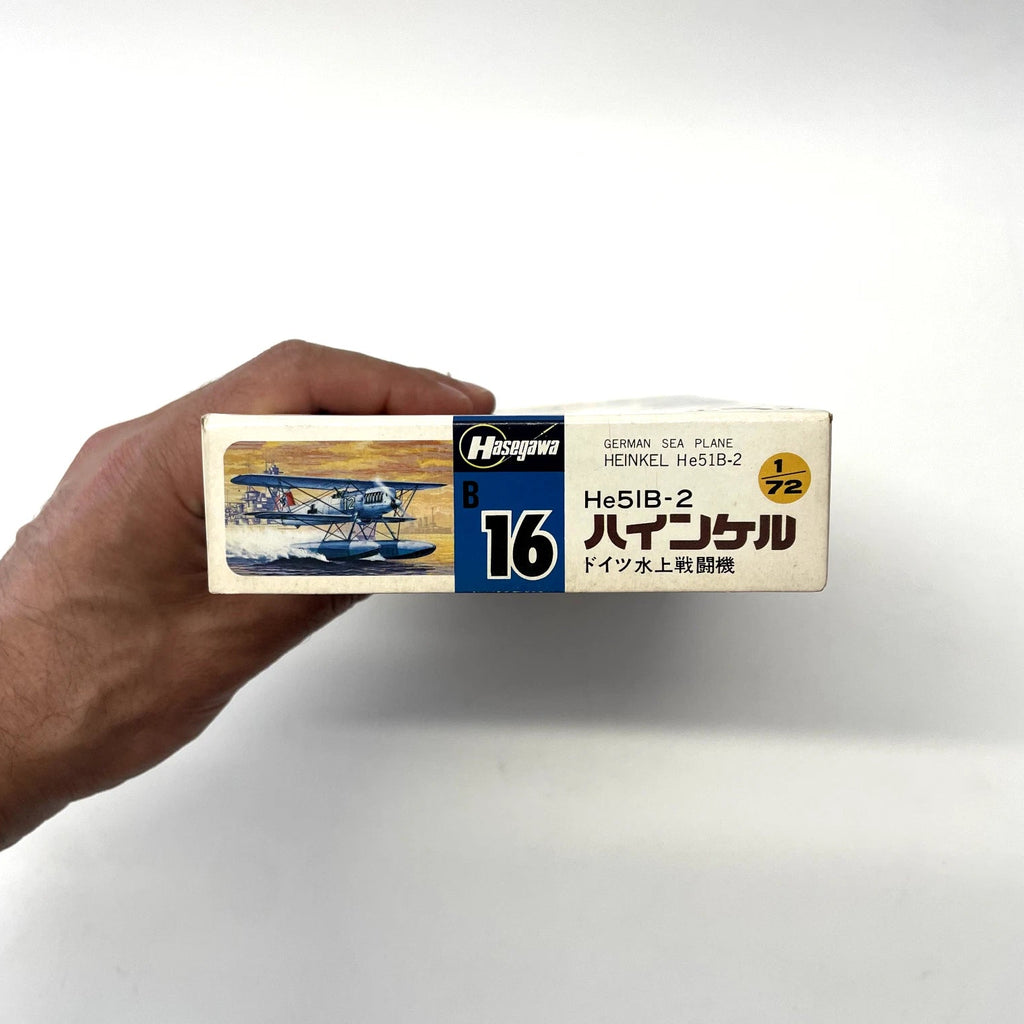 Hand holding a model airplane kit box with German sea plane illustration on a white background