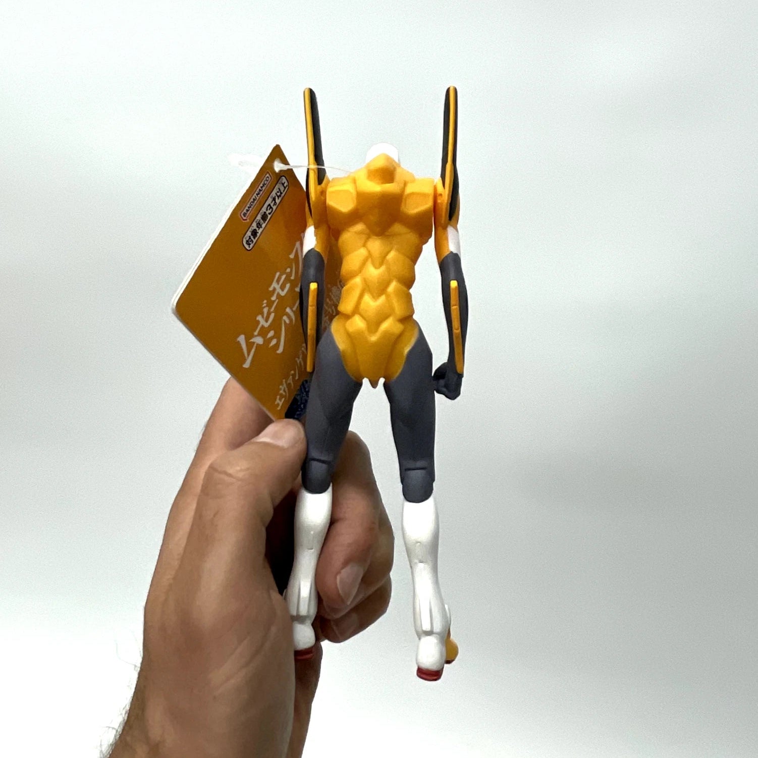 Hand holding a yellow and black action figure with a white background