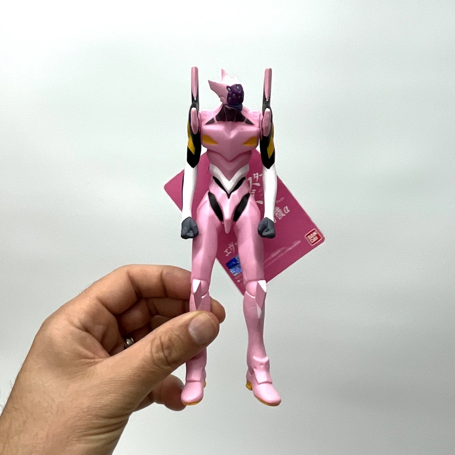 Pink robot toy figure held by a hand against a white background