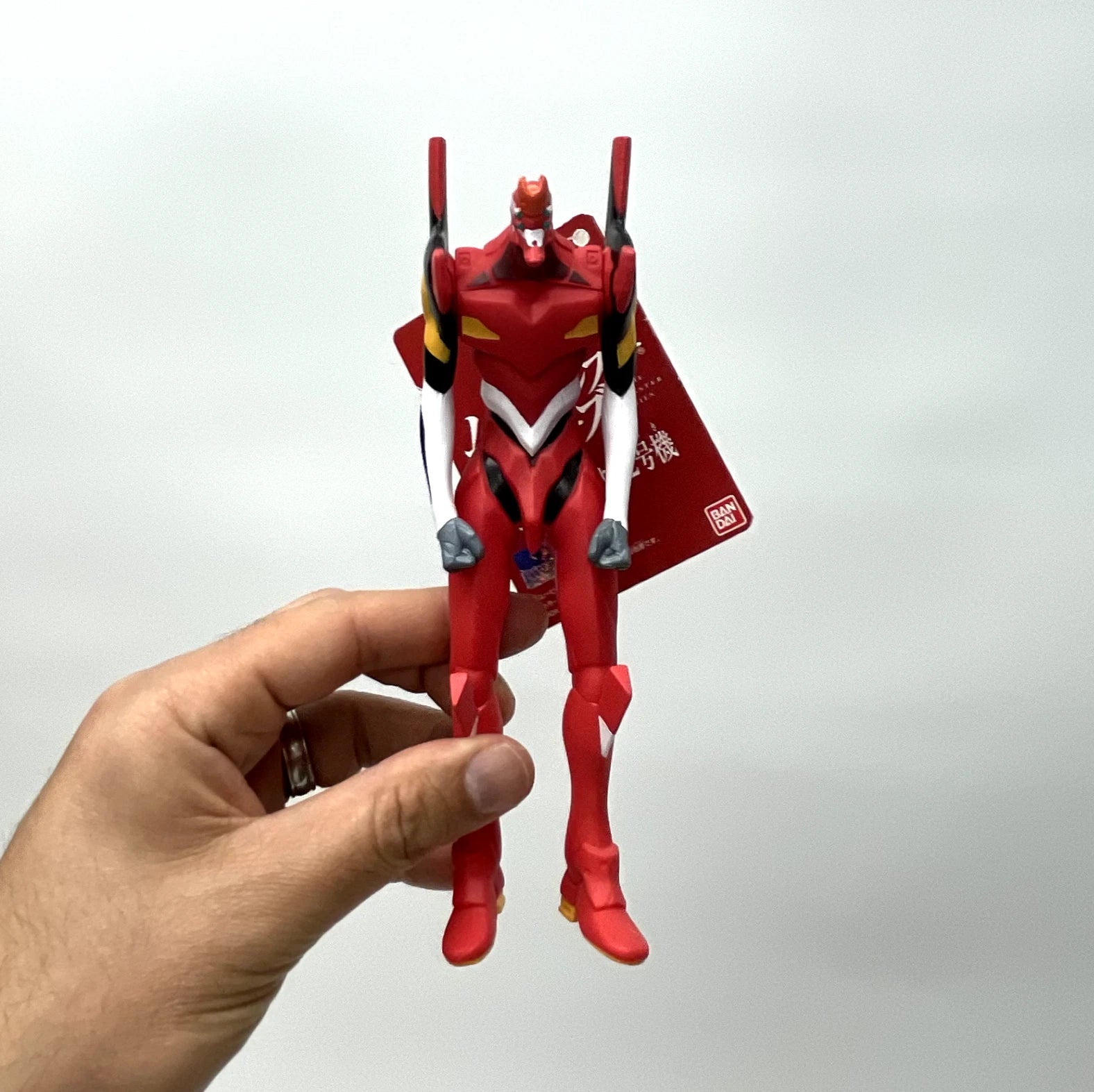 Red robot toy with a visible Bandai logo held by a hand against a white background