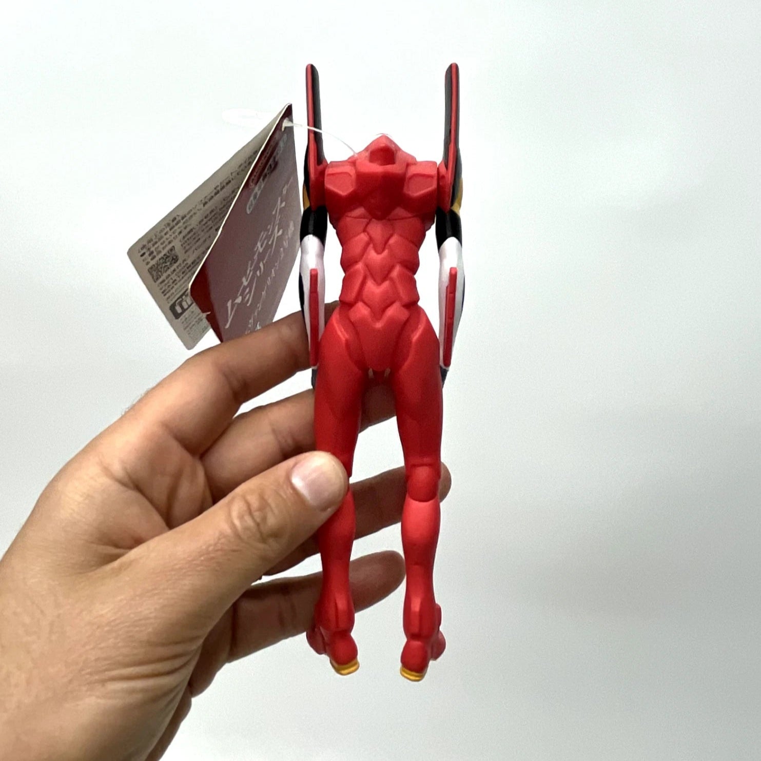 Red figurine held by a hand against a white background